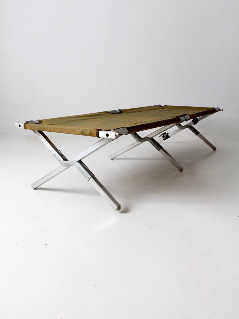 Vintage Folding Cot with Metal Frame and Green Canvas: Vintage Folding Cot with Metal Frame and Green Canvas Discover this vintage folding cot, showcasing a sturdy metal x-frame complemented by end bars and a durable green nylon canvas top. This piece is