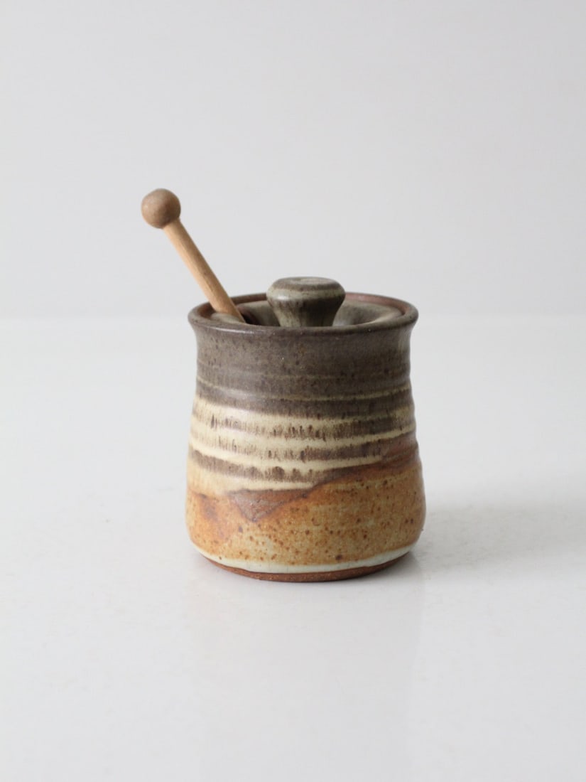 Handcrafted Vintage Studio Pottery Honey Jar with Dipper: Handcrafted Vintage Studio Pottery Honey Jar with Dipper This vintage studio pottery honey jar features a handcrafted design with a warm, earthy glaze and a unique striped pattern. The accompanying wo