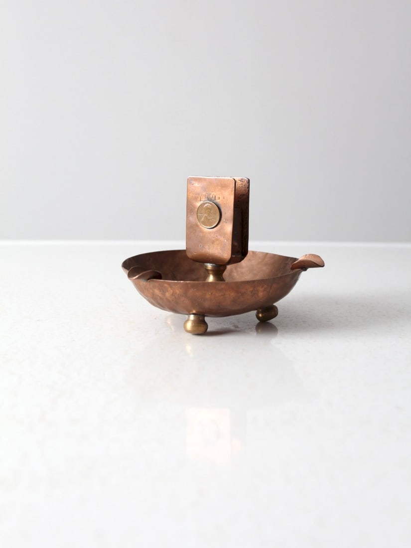 Antique Copper Ashtray with Match Holder and 1911 Penny Detail: Antique Copper Ashtray with Match Holder and 1911 Penny Detail This exquisite antique copper ashtray doubles as a match holder, showcasing a unique hammered design. The bowl is supported by three pede