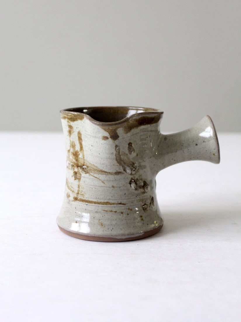 Rustic Vintage Studio Pottery Pitcher Hand-Thrown Artisan Charm: Rustic Vintage Studio Pottery Pitcher Hand-Thrown Artisan Charm This vintage studio pottery pitcher showcases rustic charm with its hand-thrown form and earthy, textured glaze. The organic shape, comp