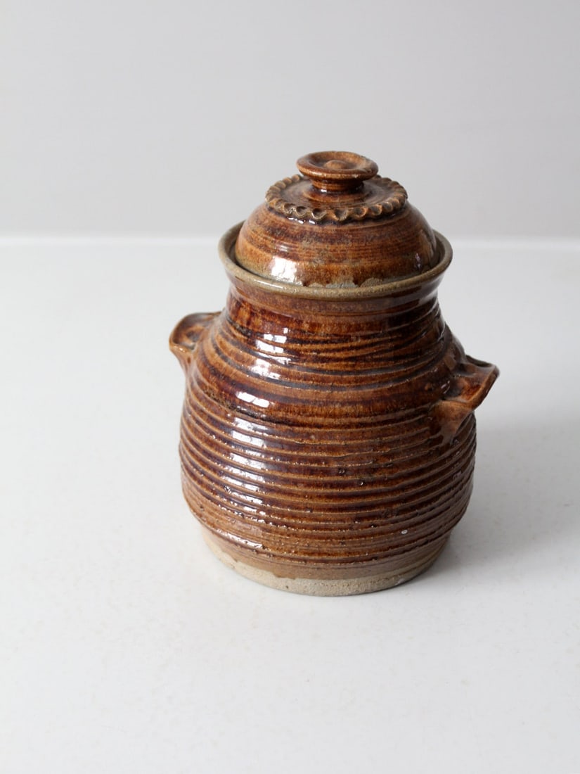 1976 Vintage Studio Pottery Jar with Striped Texture and Artist Signature: 1976 Vintage Studio Pottery Jar with Striped Texture and Artist Signature This vintage studio pottery jar, crafted in 1976, showcases a stunning rich brown glaze and features a textured striped body c