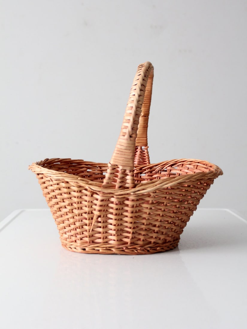 Open Weave Vintage Wicker Basket With Arched Handle and Soft Pink Hue: Open Weave Vintage Wicker Basket With Arched Handle and Soft Pink Hue This vintage wicker gathering basket features an open weave design and a wrapped arched handle. The basket displays a warm tone wi