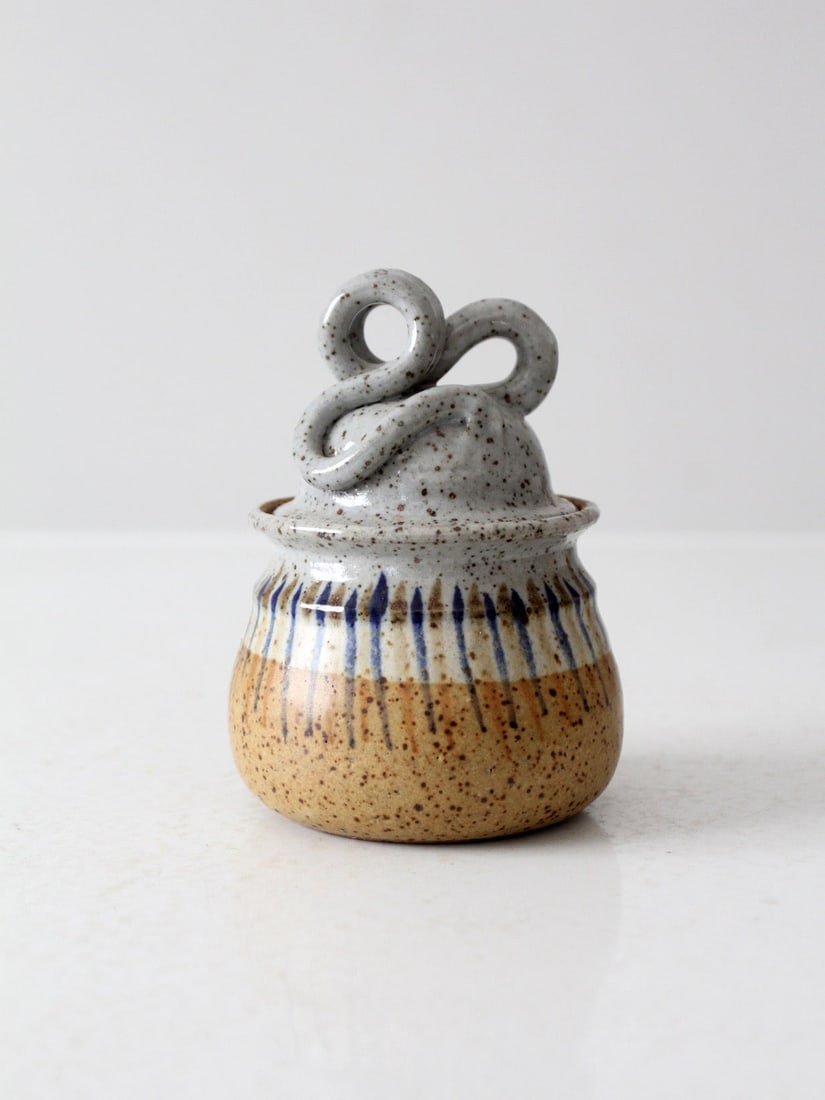 Artistic Vintage Studio Pottery Jar with Sculptural Handle: Artistic Vintage Studio Pottery Jar with Sculptural Handle This vintage studio pottery jar showcases a unique sculptural handle on its fitted lid, complemented by a subtly textured, handmade form. The