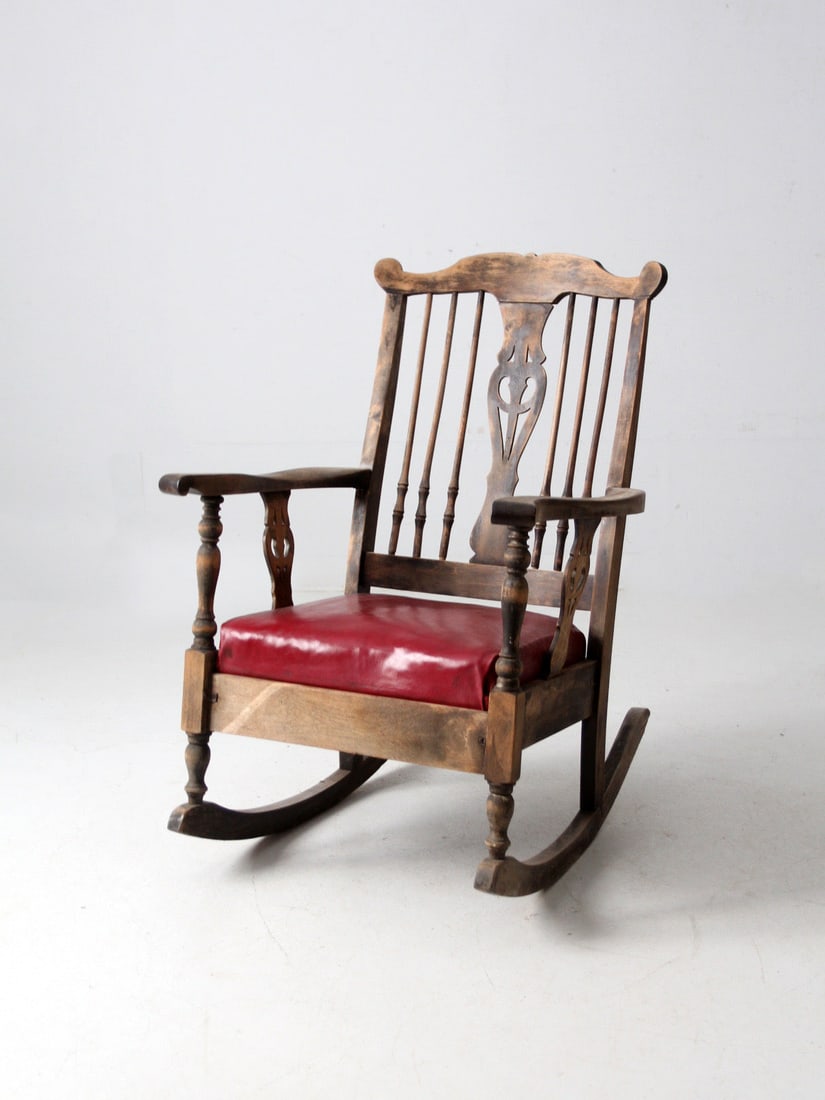 Early 1900s Farmhouse Rocker with Red Upholstered Vinyl Seat: Early 1900s Farmhouse Rocker with Red Upholstered Vinyl Seat This antique wooden rocking chair, dating to the early 1900s, features turned spindles, a carved back splat, and gracefully curved runners.
