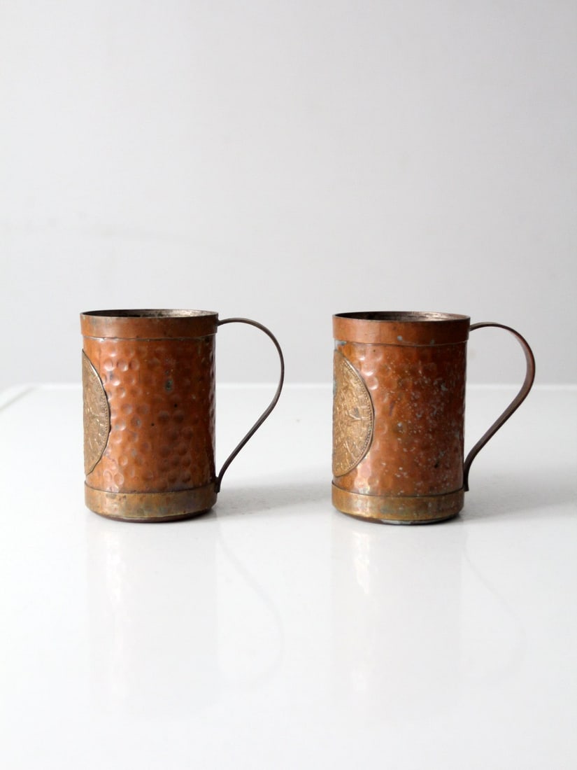 Pair of Copper Plated Mugs with Embossed Aztec Calendar Medallions: Pair of Copper Plated Mugs with Embossed Aztec Calendar Medallions This vintage pair of copper-plated mugs features a softly hammered surface and embossed Aztec calendar medallions. The warm copper to
