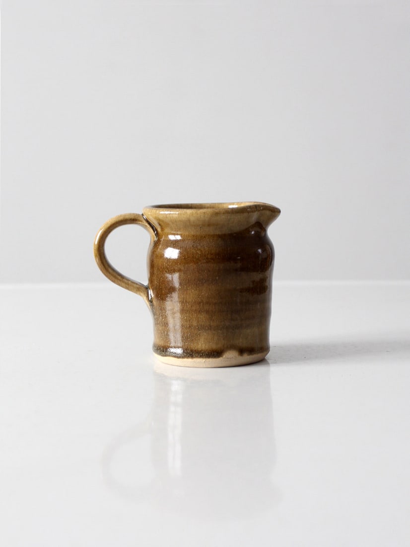 Dodge Station Pottery Creamer by Jeff Napp 1984 Olive Brown Glaze: Dodge Station Pottery Creamer by Jeff Napp 1984 Olive Brown Glaze This vintage Dodge Station Pottery creamer, crafted in 1984, is a charming piece that showcases the artistry of Jeff Napp. Hand-thrown