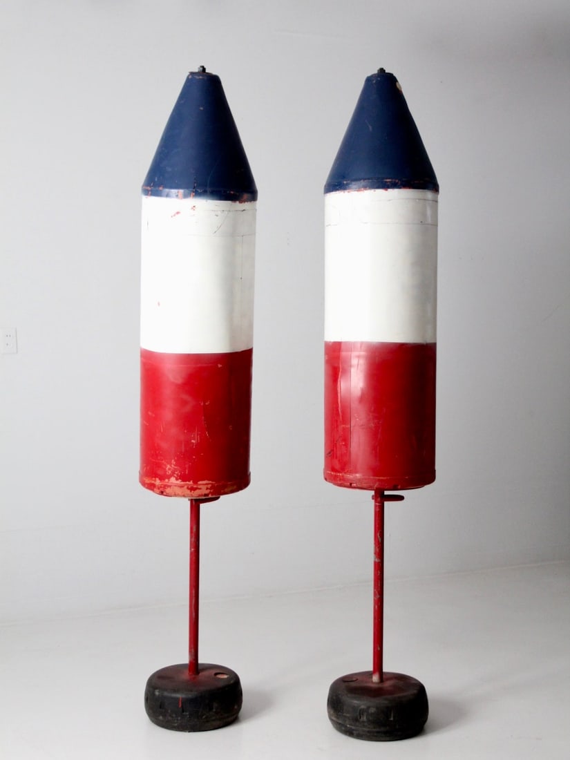 Large Vintage Red White Blue Torpedo Buoys 7 Feet Display Pair: Large Vintage Red White Blue Torpedo Buoys 7 Feet Display Pair This striking pair of large vintage buoys showcases a classic red, white, and blue torpedo shape, enhanced by sturdy red metal stands and