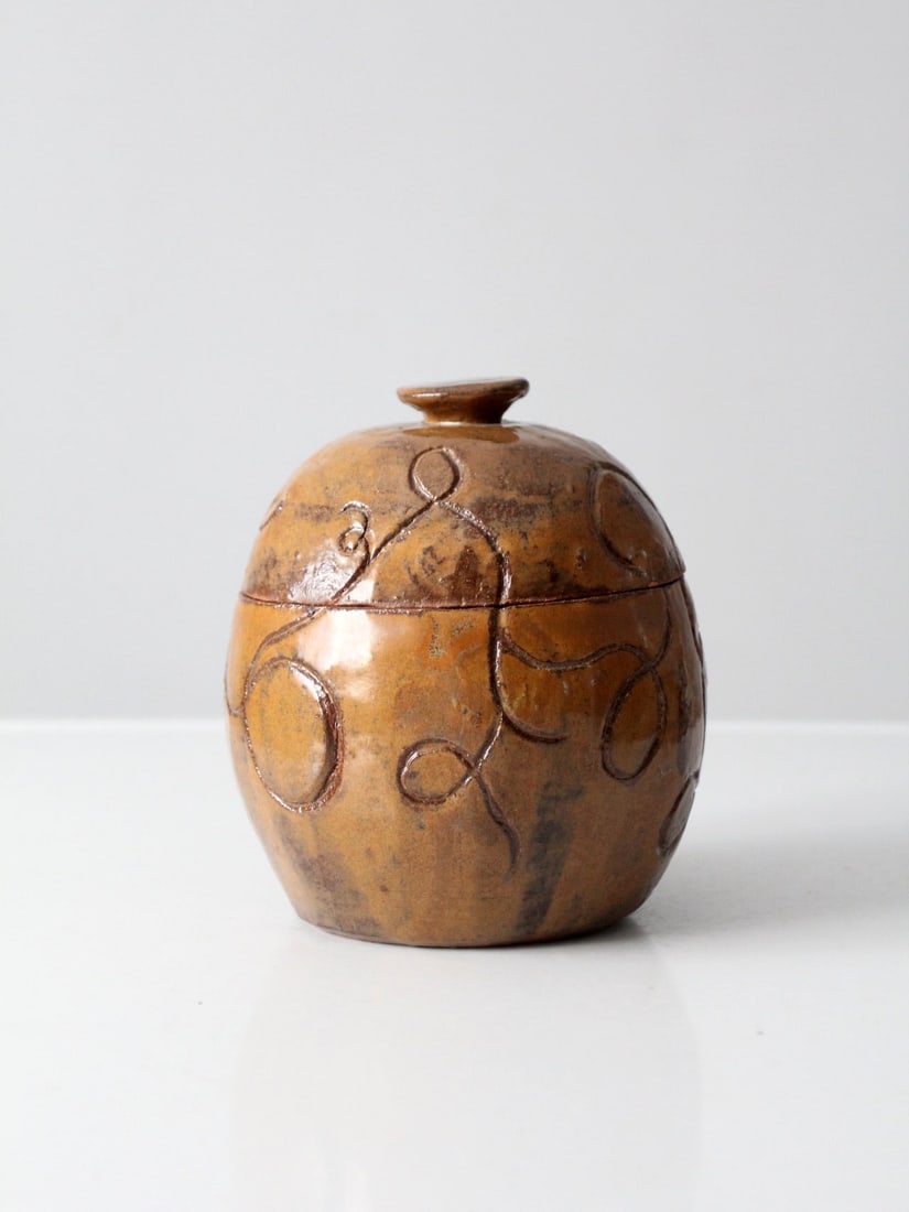 S. Miller Vintage Studio Pottery Jar with Knobbed Lid: S. Miller Vintage Studio Pottery Jar with Knobbed Lid This vintage studio pottery jar showcases the artistry of S. Miller, featuring a beautiful tawny brown glaze adorned with an etched abstract desig