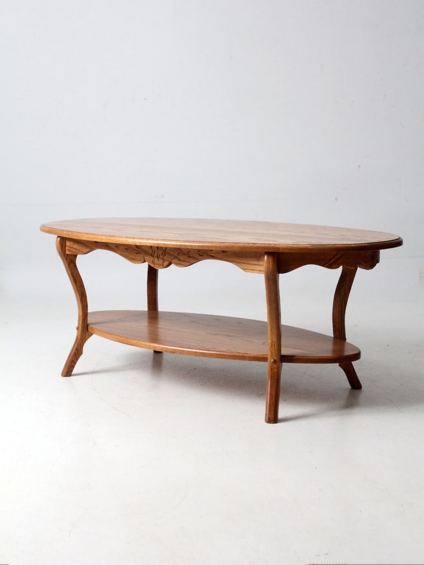 Oak Coffee Table with Oval Top and Wheat Carved Apron Colonial Revival: Oak Coffee Table with Oval Top and Wheat Carved Apron Colonial Revival This vintage oak coffee table showcases softly curved legs and a carved wheat sheaf apron, complemented by an oval top and a lowe