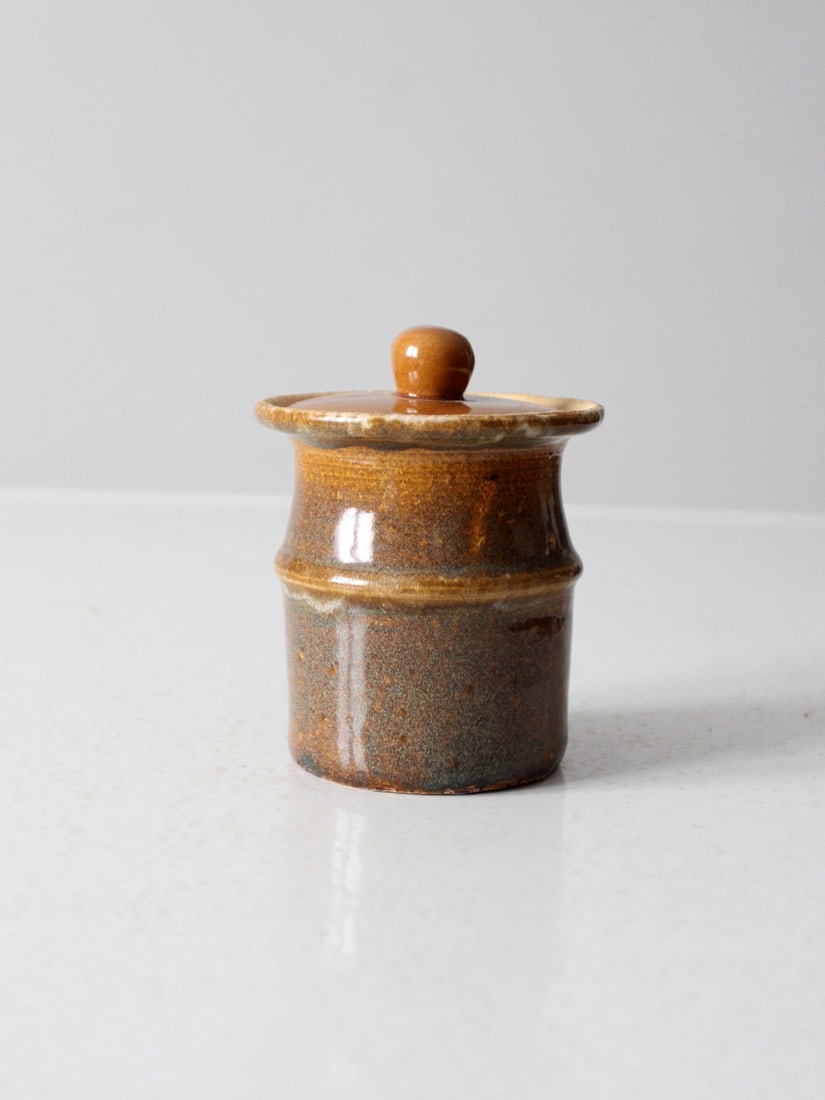 Handmade Vintage Studio Pottery Jar with Earthy Brown Glaze: Handmade Vintage Studio Pottery Jar with Earthy Brown Glaze This vintage studio pottery jar is a charming handmade piece showcasing a rich, variegated earthy brown glaze. Its lid features a bulbous ro