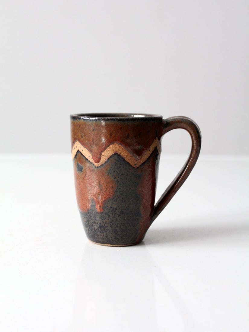 Handcrafted Vintage Studio Pottery Mug Signed Unique Design: Handcrafted Vintage Studio Pottery Mug Signed Unique Design This vintage studio pottery mug showcases a unique hand-crafted design. It features a warm brown glaze complemented by black accents and a d