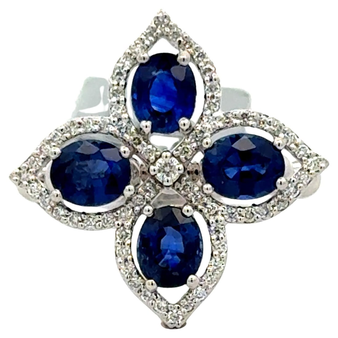 18K White Gold Sapphire and Diamond Cluster Halo Cocktail Ring 2.24 CTTW: 18K White Gold Sapphire and Diamond Cluster Halo Cocktail Ring 2.24 CTTW This elegant cocktail ring features four oval blue sapphires, totaling approximately 2.00 carats, arranged in a cross-floral cl