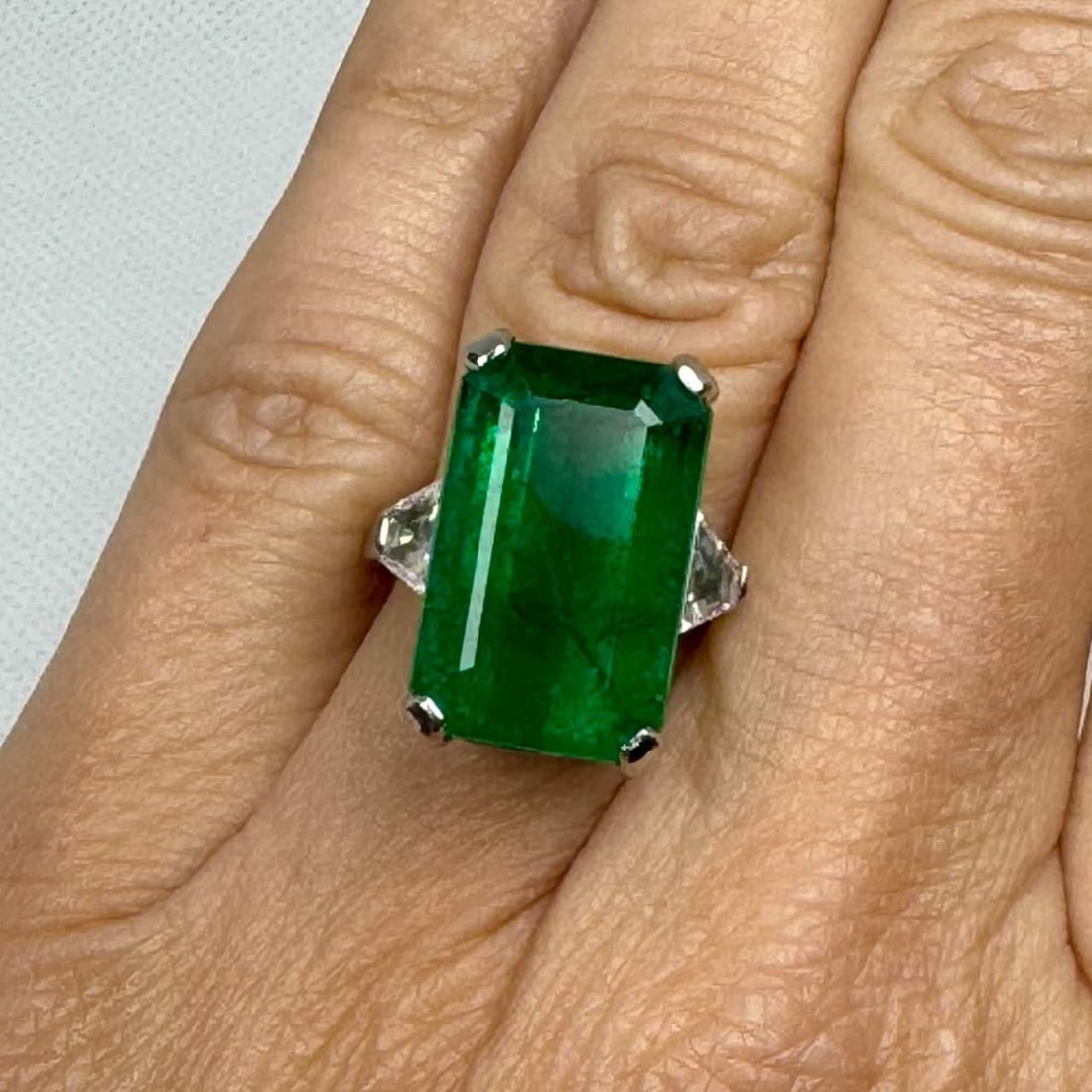 Elegant 12.00 Ct Emerald and Platinum Ring with Diamonds: Elegant 12.00 Ct Emerald and Platinum Ring with Diamonds Stunning Emerald Ring featuring an approximate 12.00 ct emerald, elegantly complemented by two trapezoid diamonds weighing approximately 0.90 c