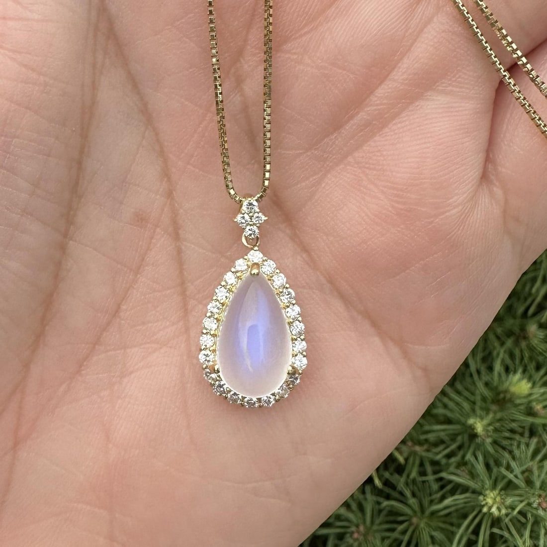 18k Yellow Gold Blue Moonstone Diamond Halo Pendant Necklace: 18k Yellow Gold Blue Moonstone Diamond Halo Pendant Necklace This stunning pendant necklace features a captivating teardrop-shaped blue moonstone, measuring 4.46 ct, set in a beautiful halo of 27 bril
