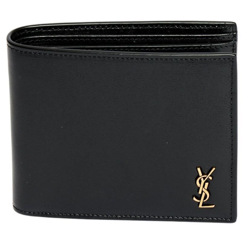 Yves Saint Laurent Black Leather Bifold Wallet with Gold Logo: Yves Saint Laurent Black Leather Bifold Wallet with Gold Logo This exquisite Yves Saint Laurent bifold wallet is crafted from premium black leather, showcasing a sleek and elegant design. It features