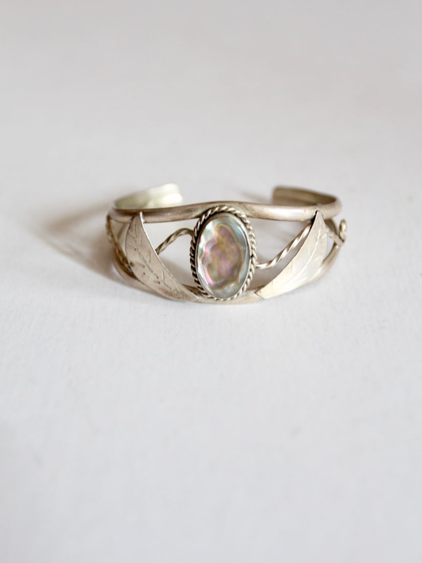 Vintage Mexican Abalone Cuff Bracelet with Alpaca Silver Details: Vintage Mexican Abalone Cuff Bracelet with Alpaca Silver Details This vintage Mexican abalone shell cuff bracelet features a striking design with alpaca silver leaves and a banner that beautifully fra