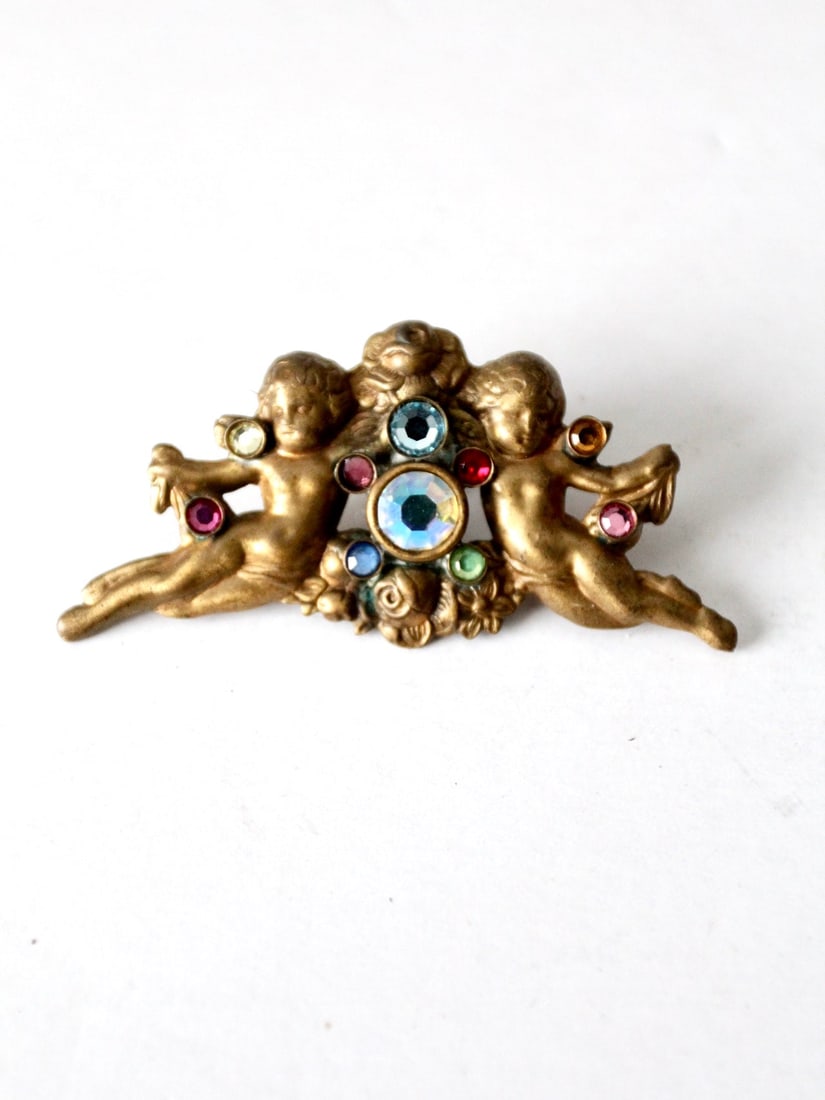 Vintage Gold Tone Rhinestone Cherubs Brooch Pin: Vintage Gold Tone Rhinestone Cherubs Brooch Pin Adorn yourself with this exquisite vintage rhinestone cherubs pin. Crafted in a radiant gold tone, this brooch showcases intricately detailed cast metal