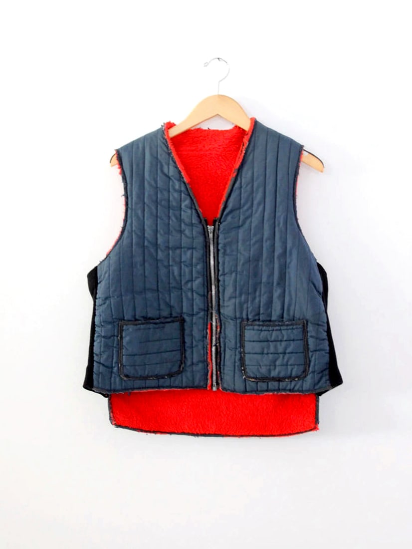 1970s Vintage Navy Blue Puffer Vest with Red Fleece Lining: 1970s Vintage Navy Blue Puffer Vest with Red Fleece Lining This vintage 1970s puffer vest is both stylish and functional, featuring a vibrant navy blue nylon exterior complemented by a cozy red woolly