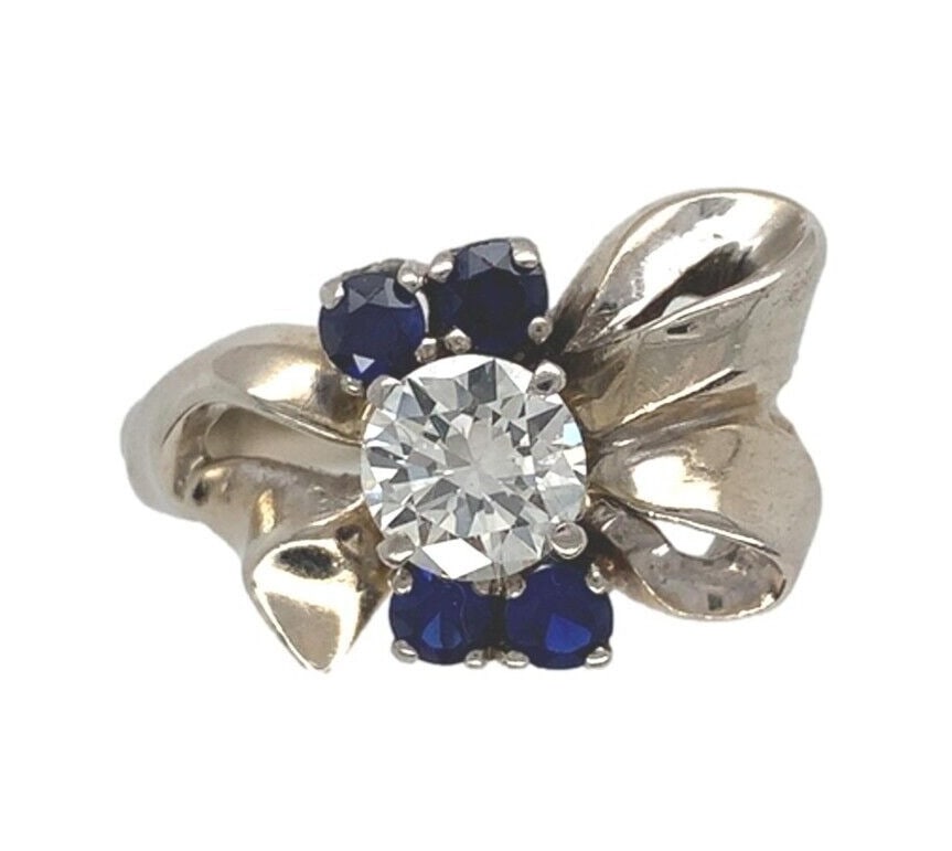Retro Era 14k White Gold Bow Ring With Diamond and Lab Sapphires Accents: Retro Era 14k White Gold Bow Ring With Diamond and Lab Sapphires Accents This retro ring from the 1930s-1940s is crafted in 14k white gold and features a European cut diamond of approximately 0.66 car