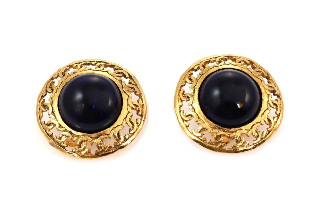 Chanel Clip On Earrings with Purple Cabochon and Gold Plated Round Logo Design: Chanel Clip On Earrings with Purple Cabochon and Gold Plated Round Logo Design These Chanel round clip-on earrings feature the iconic logo design with a dark purple cabochon stone set in yellow gold-p