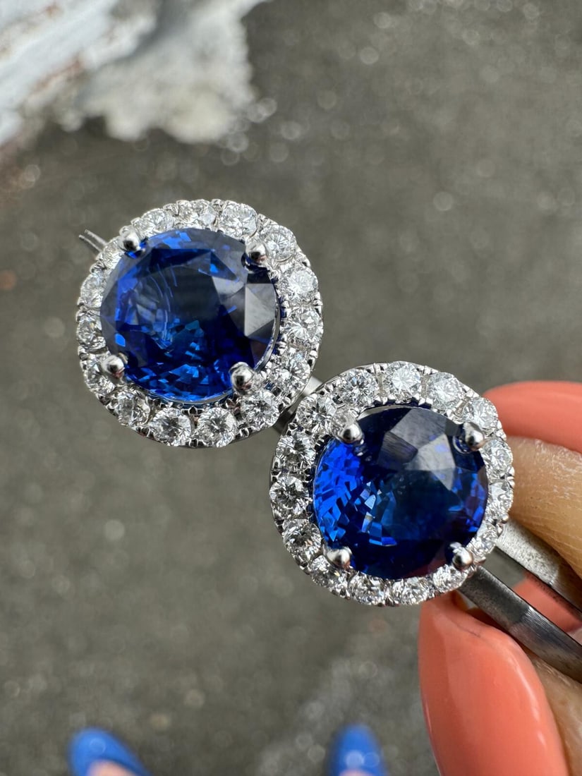 New 18k White Gold GIA Round Blue Sapphire Diamond Halo Stud Earrings: New 18k White Gold GIA Round Blue Sapphire Diamond Halo Stud Earrings Elevate your elegance with these exquisite 18k Gold stud earrings featuring a stunning combination of vivid blue sapphires and spa