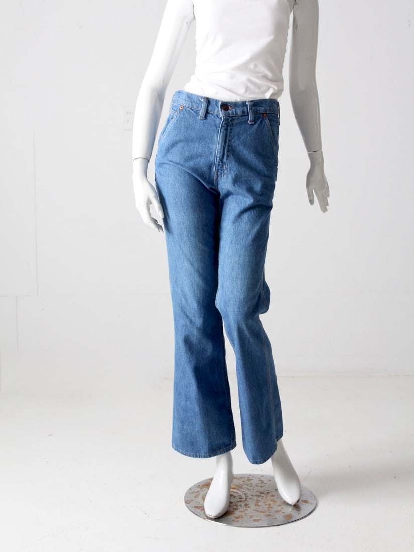 1970s Vintage Levis Flare Jeans with Orange Feather Tab: 1970s Vintage Levis Flare Jeans with Orange Feather Tab Discover a classic pair of 1970s vintage Levis jeans featuring a stylish flare leg design and high waist. These jeans are equipped with a belt b