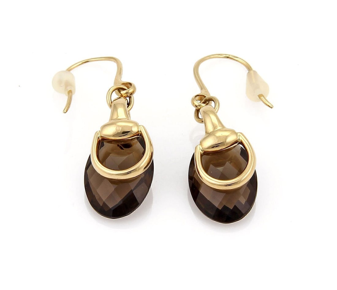 18k Yellow Gold Horsebit Dangle Earrings with Smokey Quartz by Gucci: 18k Yellow Gold Horsebit Dangle Earrings with Smokey Quartz by Gucci These dangle earrings feature a hook closure and are crafted from 18k yellow gold. Each earring showcases a smokey quartz stone set