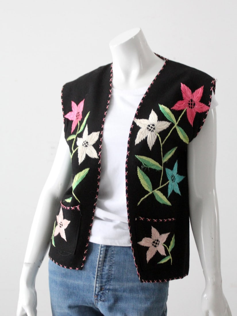 1950s Vintage Mexican Hand-Embroidered Floral Vest: 1950s Vintage Mexican Hand-Embroidered Floral Vest This vintage 1950s Mexican vest showcases vibrant hand-embroidery on a black felt background, featuring a colorful floral design in white, pink, blue