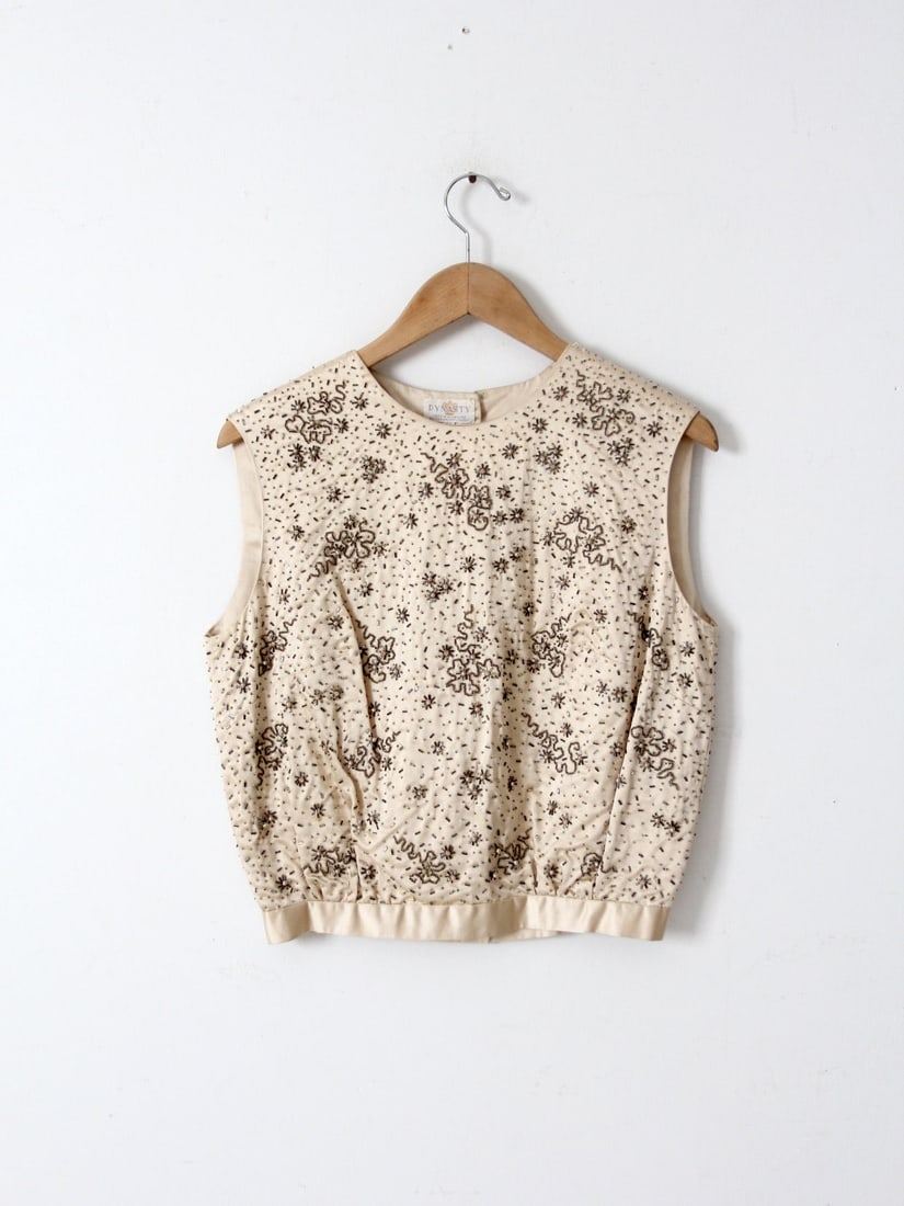 1960s Dynasty Cream Silk Beaded Sleeveless Blouse: 1960s Dynasty Cream Silk Beaded Sleeveless Blouse This exquisite early 1960s vintage Dynasty blouse is a true statement piece. Crafted from luxurious cream silk, this sleeveless top showcases stunning