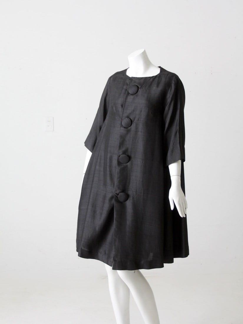 1960s Vintage Black Silk Trapeze Coat with Oversized Buttons: 1960s Vintage Black Silk Trapeze Coat with Oversized Buttons Step back in time with this stunning 1960s vintage silk trapeze coat. Crafted from luxurious black silk, this coat features a trapeze or sw