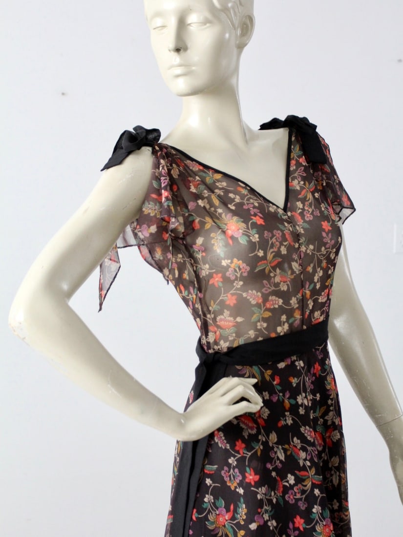 1970s Vintage Floral Print Handkerchief Hem Dress: 1970s Vintage Floral Print Handkerchief Hem Dress Step back in time with this stunning 1970s vintage handkerchief hem dress, featuring a captivating floral print on a sheer black fabric. This chic dre