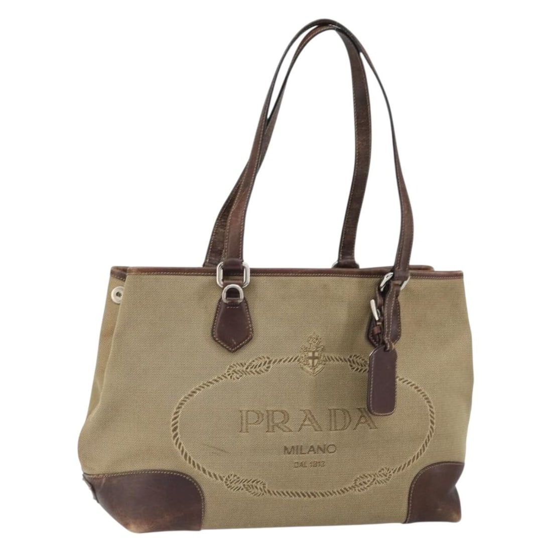 Beige Silver Canvas Tote PRADA Italy with Name Tag: Beige Silver Canvas Tote PRADA Italy with Name Tag This PRADA tote bag features a beige and silver canvas exterior and includes a name tag accessory. The bag is made in Italy and has a handle drop of