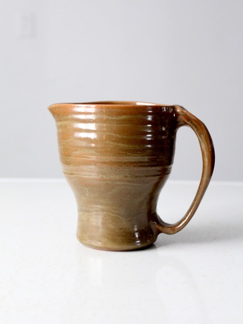 Hand-Thrown Vintage Studio Pottery Pitcher Signed Rustic Elegance: Hand-Thrown Vintage Studio Pottery Pitcher Signed Rustic Elegance This stunning vintage studio pottery pitcher features a hand-thrown design and a beautiful organic glaze, adding rustic elegance to yo