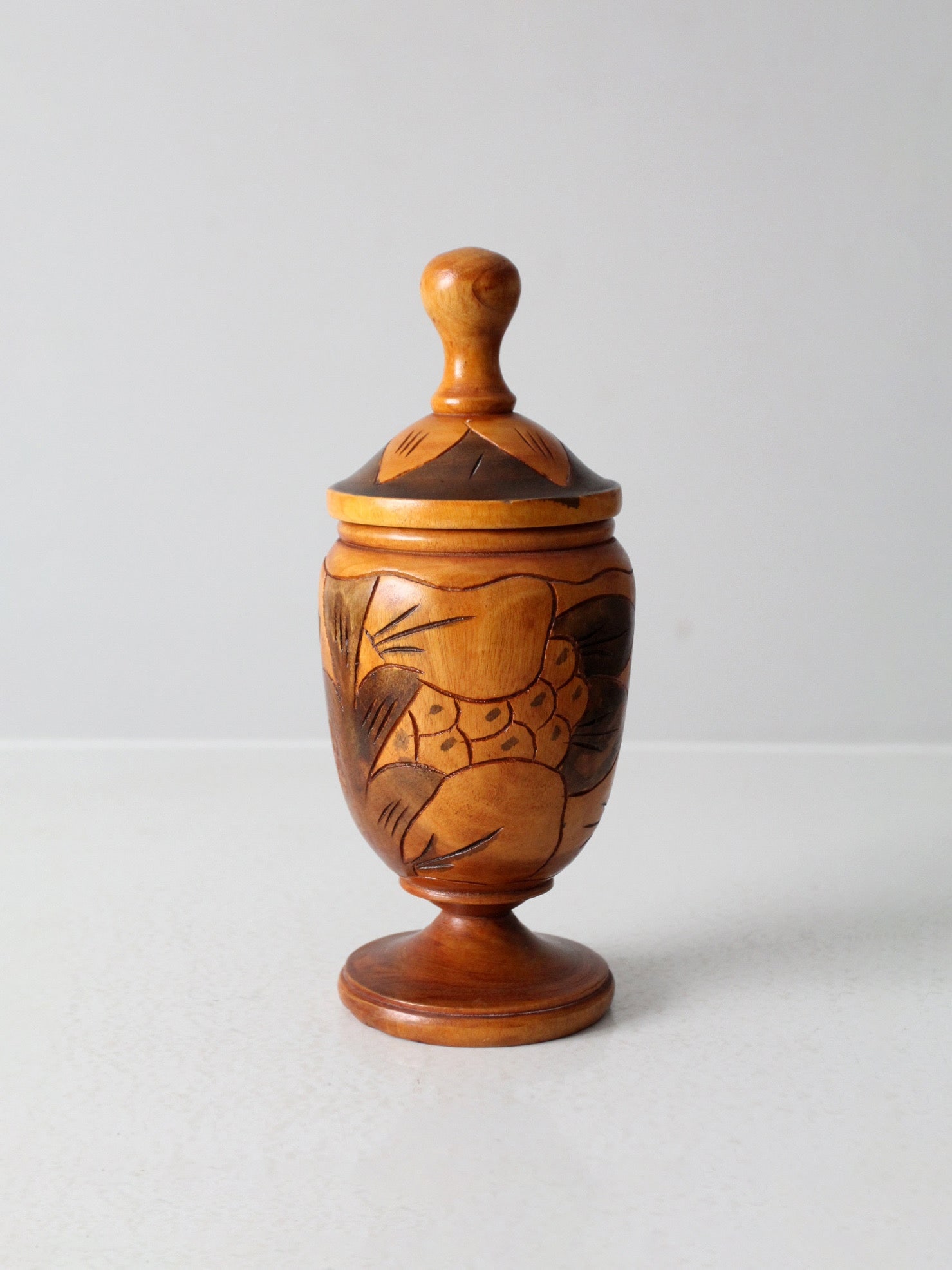 Vintage Hand-Carved Wooden Storage Jar with Lid: Vintage Hand-Carved Wooden Storage Jar with Lid This vintage hand-carved wooden jar showcases intricate stylized botanical carvings inspired by tropical foliage, beautifully highlighted by warm, natur
