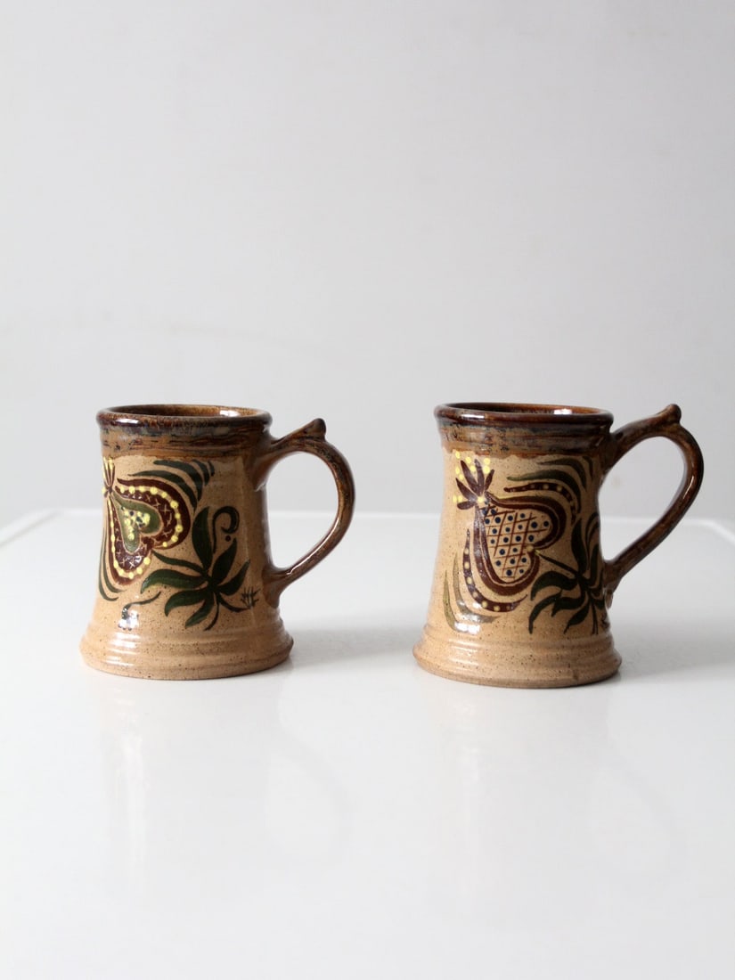 Pair of Handcrafted Floral Studio Pottery Mugs with Earthy Glaze: Pair of Handcrafted Floral Studio Pottery Mugs with Earthy Glaze This pair of vintage studio pottery mugs features hand-painted floral motifs and warm, earthy glaze tones. Each mug displays subtle var