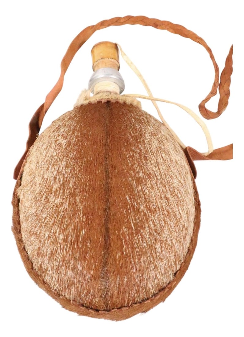 Hide Wrapped Aluminum Water Jug with Leather Strap Circa 1970s: Hide Wrapped Aluminum Water Jug with Leather Strap Circa 1970s This vintage canteen features a hide-covered exterior over a durable aluminum body, complemented by a woven leather carrying strap. Likel