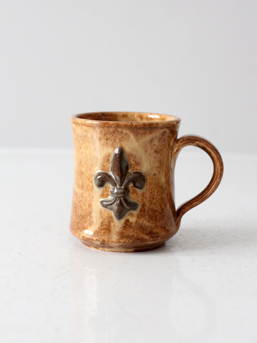 Vintage Studio Pottery Mug with Fleur-De-Lis Design: Vintage Studio Pottery Mug with Fleur-De-Lis Design This vintage studio pottery mug features a beautifully raised fleur-de-lis motif on one side, making it an elegant addition to any collection. The g
