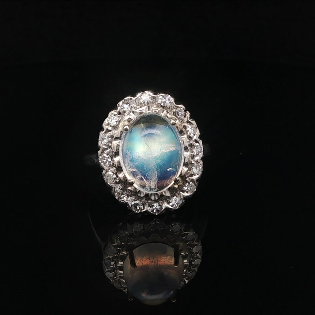 White Gold Rainbow Moonstone and Single Cut Diamond Vintage Halo Ring: White Gold Rainbow Moonstone and Single Cut Diamond Vintage Halo Ring This vintage ring features a natural oval cabochon-cut rainbow moonstone, prong-set at the center and surrounded by a halo of sixt