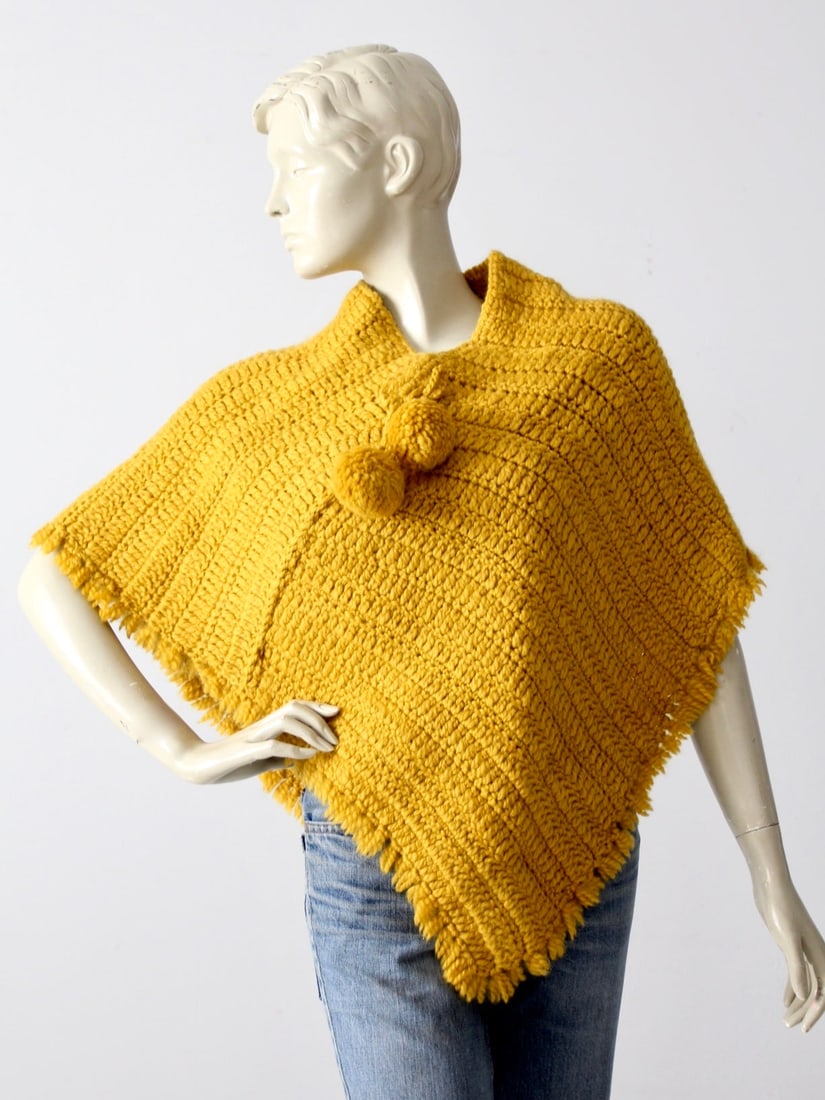 1960s Vintage Hand-Knit Mustard Yellow Poncho with Fringed Hem: 1960s Vintage Hand-Knit Mustard Yellow Poncho with Fringed Hem This vintage 1960s hand-knit poncho from our Stylist's Collection is a unique addition to any wardrobe. Crafted in a vibrant mustard yell