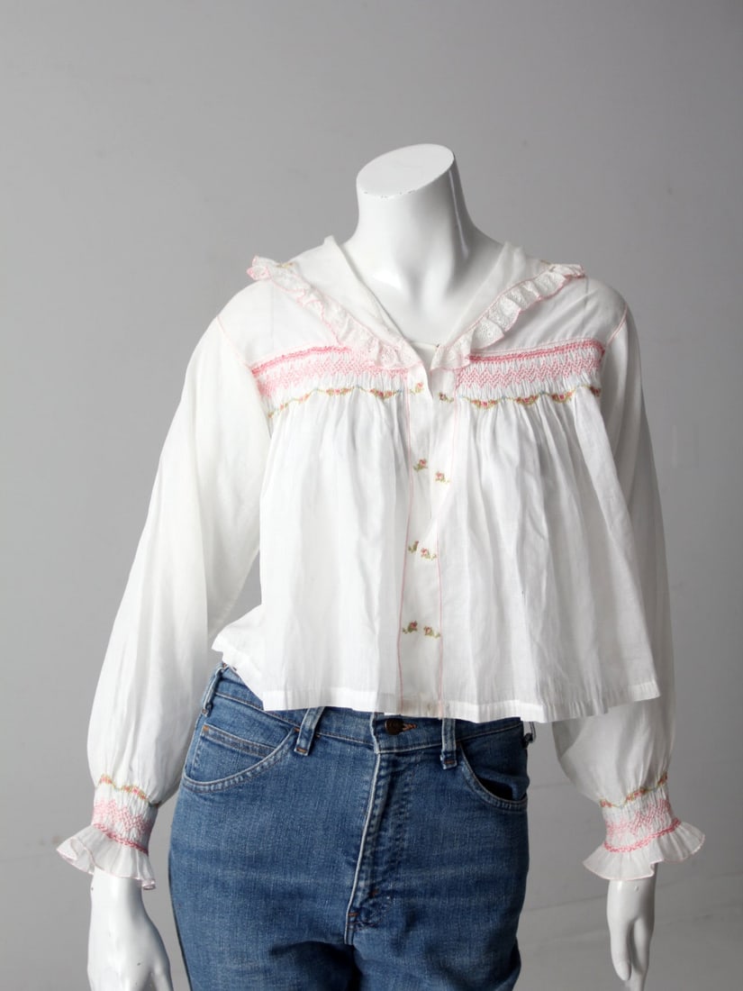 Early 20th Century Antique Smocked Blouse with Floral Embroidery: Early 20th Century Antique Smocked Blouse with Floral Embroidery Explore this exquisite early 20th century antique embroidered smocked blouse, crafted from sheer white cotton. This charming top featur