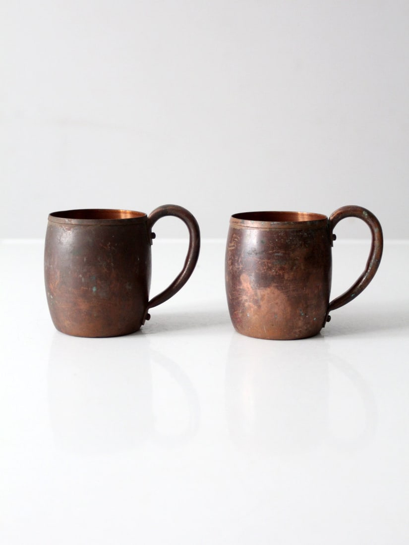 Pair of Classic Vintage Copper Drinking Mugs with Riveted Handles: Pair of Classic Vintage Copper Drinking Mugs with Riveted Handles This pair of vintage copper mugs features a classic utilitarian design with softly rounded bodies and riveted handles. The naturally a