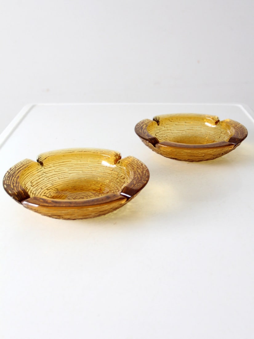 Vintage Anchor Hocking Soreno Honey Gold Glass Ashtray Pair: Vintage Anchor Hocking Soreno Honey Gold Glass Ashtray Pair Enhance your decor with this charming pair of vintage Anchor Hocking Soreno ashtrays. Crafted from stunning honey gold glass, each piece sho