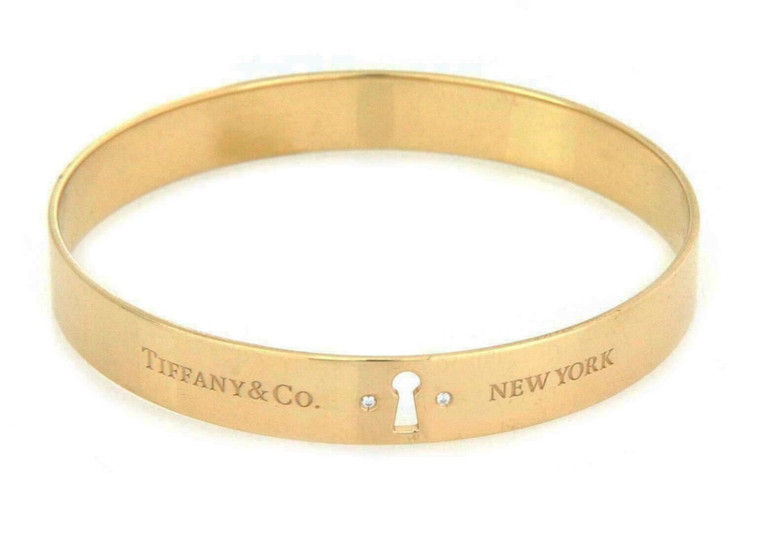 18k Yellow Gold Keyhole Lock Bangle by Tiffany & Co.: 18k Yellow Gold Keyhole Lock Bangle by Tiffany & Co. This Tiffany & Co. keyhole lock bangle bracelet is expertly crafted from solid 18k yellow gold, showcasing a sleek and modern design highlighted by