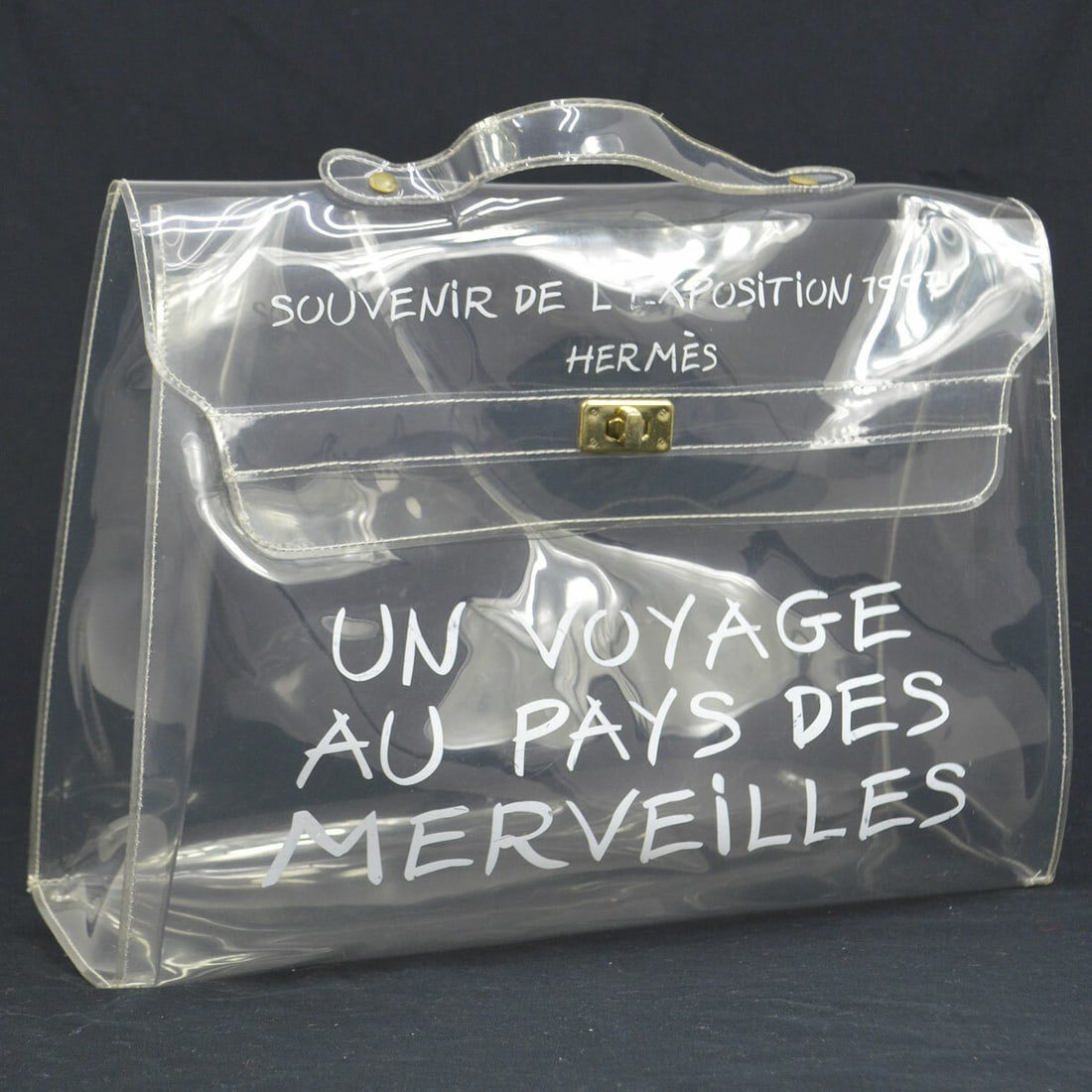HERMES Vinyl Kelly Beach Handbag 1997 Souvenir Exhibition: HERMES Vinyl Kelly Beach Handbag 1997 Souvenir Exhibition Introducing the Hermes Vinyl Kelly Beach Handbag, a delightful accessory perfect for casual outings. This medium-sized handbag features a clea