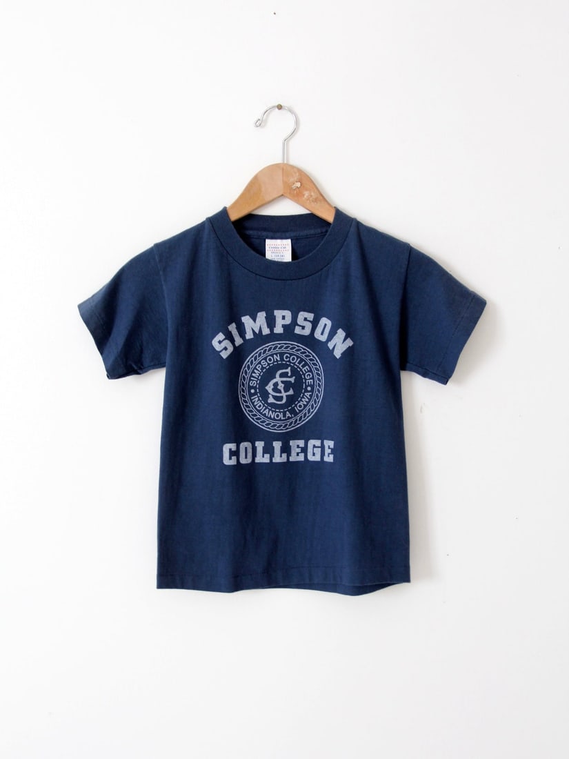 1980s Vintage Simpson College Navy T-Shirt Cotton Tee: 1980s Vintage Simpson College Navy T-Shirt Cotton Tee Celebrate your school spirit with this vintage 1980s Simpson College t-shirt. Crafted from 100% cotton, this navy blue tee features a striking whi