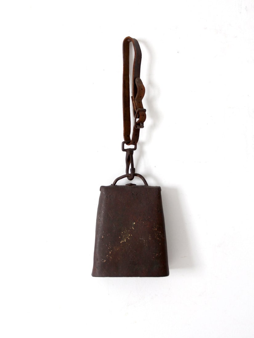 Rustic Antique Cow Bell with Leather Strap 4 x 3.12 x 7.75: Rustic Antique Cow Bell with Leather Strap 4 x 3.12 x 7.75 This antique cow bell showcases a leather buckled strap, exuding rustic charm and character. The weathered patina and aged leather contribute
