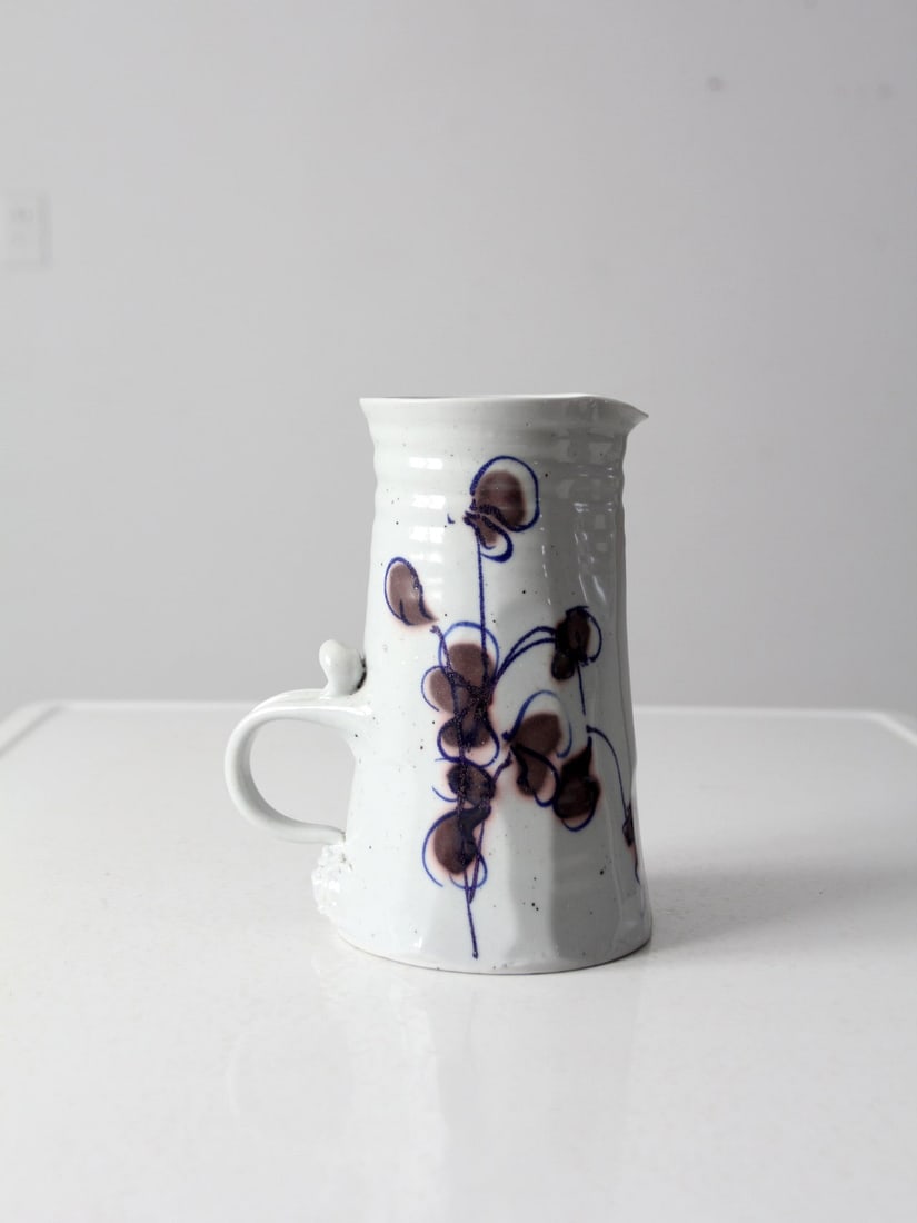 Signed Vintage Studio Pottery Pitcher with Floral Design 8.5": Signed Vintage Studio Pottery Pitcher with Floral Design 8.5" This vintage studio pottery pitcher is a beautifully crafted ceramic ewer, signed by the artist. It features a low-set handle and is adorn