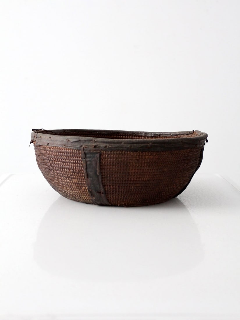 Handwoven West African Bowl with Leather Trim and Coiled Design: Handwoven West African Bowl with Leather Trim and Coiled Design This vintage West African woven bowl features a compact, coiled construction with a leather-bound rim and base. The bowl displays a rich