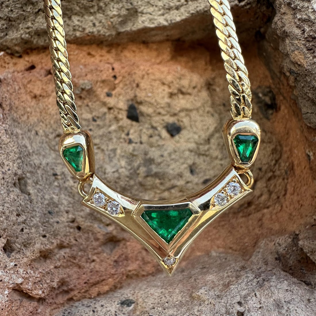 V Necklace with Muzo Colombian Emeralds Diamonds in 18k Yellow Gold Flat Curb Chain: V Necklace with Muzo Colombian Emeralds Diamonds in 18k Yellow Gold Flat Curb Chain This elegant necklace features a V-shaped design set with three natural Muzo Colombian emeralds in vivid green hues,