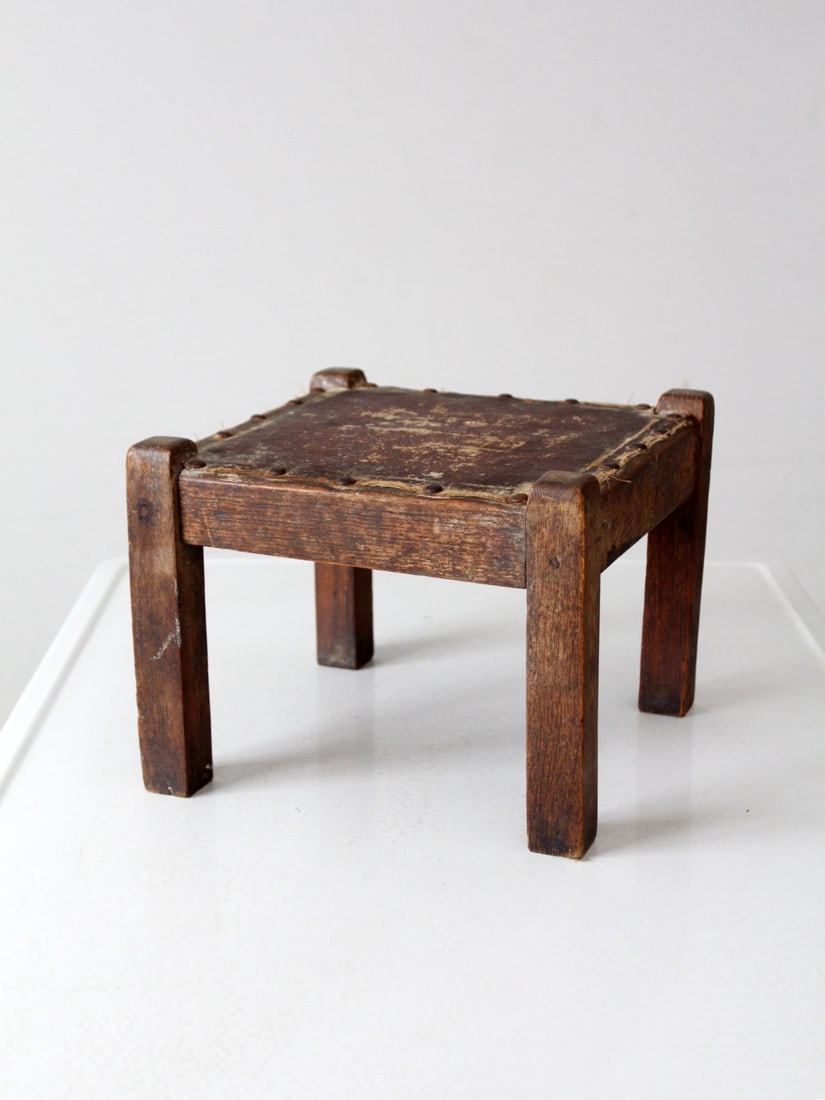 Turn of the Century Upholstered Wood Footstool Accent: Turn of the Century Upholstered Wood Footstool Accent This charming turn of the century wood footstool boasts a classic square silhouette and a gently worn upholstered top. Crafted from dark wood, it 